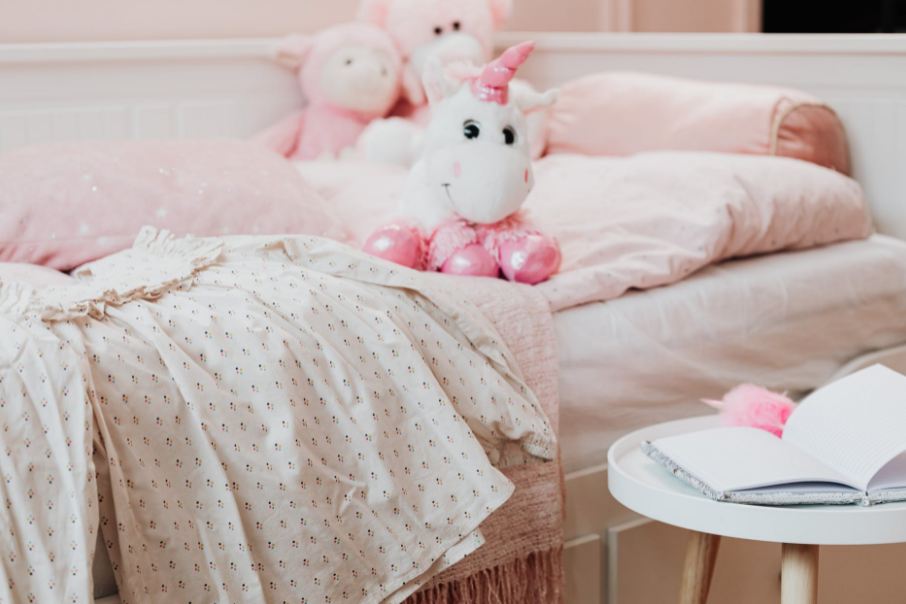 White and pink unicorn plush on a bed. 