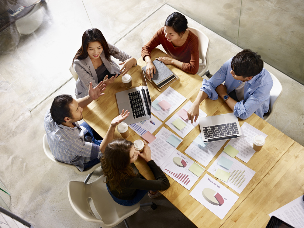 High angle view of a team of Asian and Caucasian corporate executives discussing business in meeting room