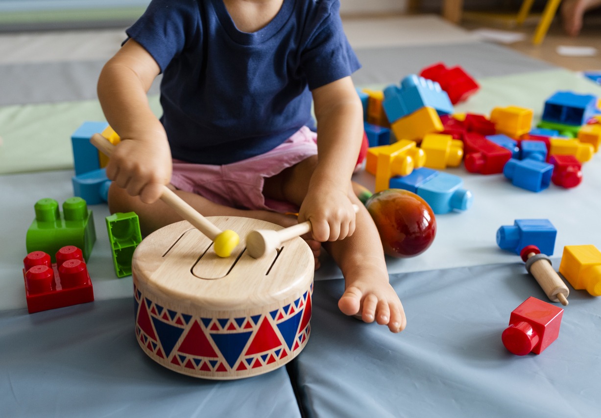 child playing with wooden drum with blocks and other toys in the background